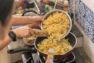 Woman cooking macaroni dish in flying pan during covid-19 quarantine.