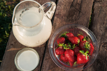 Fresh strawberries on plate on old wooden background. Red tulips in vase on table. Jar and glass of milk. Breakfast time. Healthy food. Vegetarian dish. Spring time
