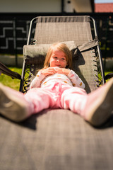 Portrait of a beautiful little 2 years old girl in red hat on sun chait in backyard