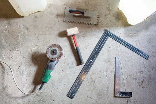 Cement floor with tools - angle grinder, construction rulers and humer are in the apartment that is under construction, remodeling, renovation, overhaul, extension, restoration and reconstruction