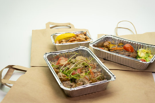 Paper bag and ready food in foil containers on a white background. Food delivery during the period of quarantine, self-isolation.