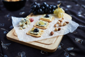Three blue cheese crackers with grapes are on a cutting board.