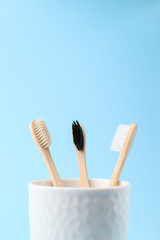 Three bamboo toothbrushes in a white glass. Zero waste and without plastic concept. Copy space, vertical orientation. Light blue background.