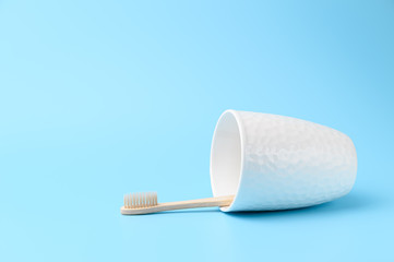 A bamboo toothbrush in a white glass lies on a light blue background. Zero waste and without plastic concept. Copy space, horizontal orientation.