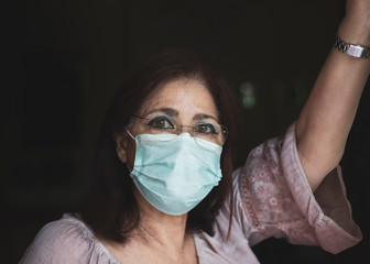 Sad lonely isolated woman stays home with a sterile protective mask on her face looking out the...