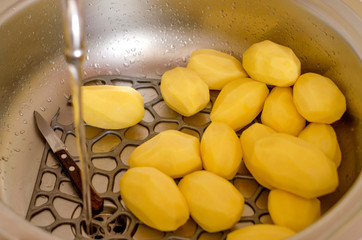 Raw peeled potatoes lie in the sink, washed under clean water. Cooking potatoes.
