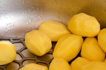 Raw peeled potatoes lie in the sink, washed under clean water. Cooking potatoes.