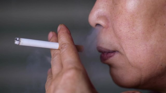 Closeup of Asian middle aged woman smoking cigarette in slow motion