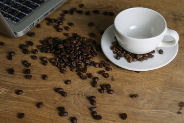 Fototapeta na wymiar White coffee cup and coffee beans on wooden table with copyspace for text. Selective focus.