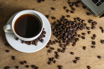 White coffee cup and coffee beans on wooden table with copyspace for text. Selective focus.