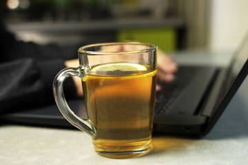 Young woman working on a laptop on the kitchen table and drinking lemon tea, remote work at home, self-isolation, selective focus