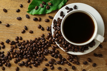 White coffee cup and coffee beans on wooden table with copyspace for text. Selective focus.