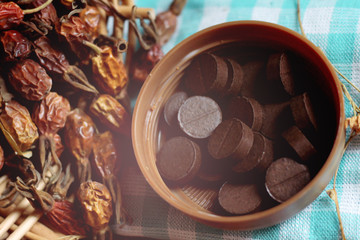 Black tablets and dry medicinal herb on wooden background