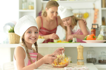 Cute girls with mother preparing delicious fresh salad in kitchen