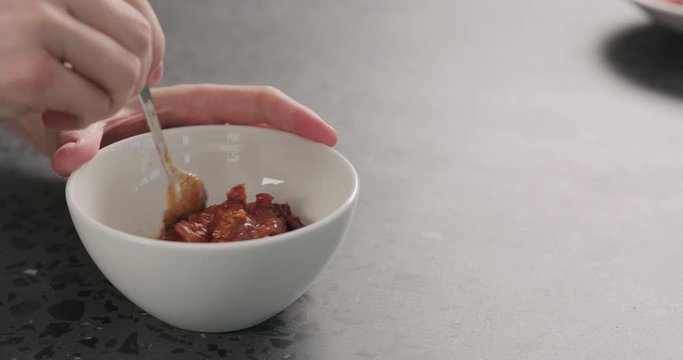 Slow motion man hand mixing tomato sauce with sun dried tomatoes in white bowl