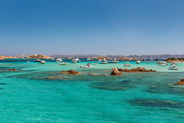 Various tourist boats are stationed in the clear and transparent waters in the Maddalena archipelago in Sardinia, Italy.