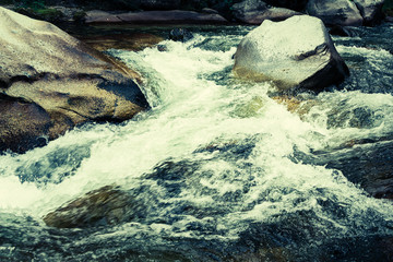 stream in stone bed, fast mountain river among rocks, water boils in eddies of current
