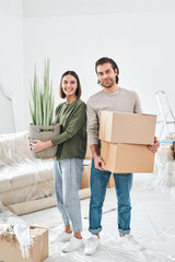 Young smiling woman with domestic plant and her husband with two packed boxes