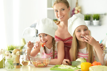 Cute girls with mother preparing delicious fresh salad in kitchen