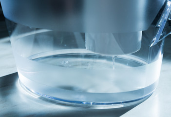 Close-up of a jug with a water purification cartridge. A stream of clear water flows from the cartridge. The concept of purification.