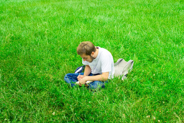 Naklejka na ściany i meble A young man sits on the grass and draws on a sketchbook.