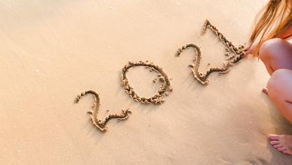 woman writting 2021 on sand beach. ocean wave and lettering on the beach. Happy New Year 2021. tropical vacation 2021.
