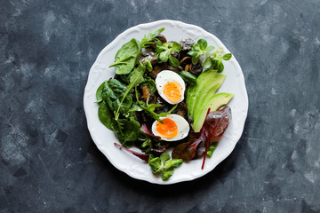 Healthy breakfast eggs, avocado, mushrooms and fresh greens arugula, spinach on a dark plate top view