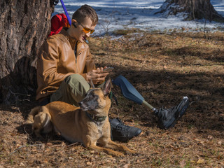 Close up photo of a man with a prosthesis rests after a long walk with his best friend - a dog from...