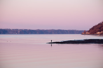 Man standing at the end of a narrow strip of beach in the St. Lawrence River during a pink sunrise in the Cap-Rouge area, Quebec City, Quebec, Canada