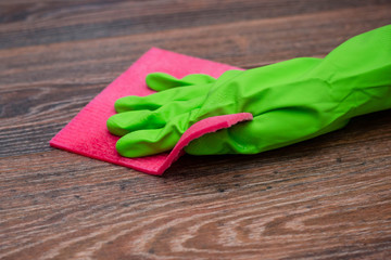 Closeup of a hand in a green rubber glove rubbing a wet wooden surface. The concept of disinfection of premises, the prevention of viral and bacterial diseases. Cleaning wooden surfaces.