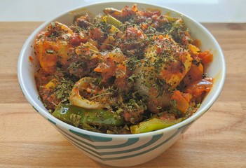 A home cooked Indian style bowl of hot and spicy capsicum and cottage cheese curry also called kadhai paneer with fenugreek garnishing on a wooden background