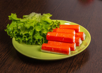 Crab sticks, parsley and lettuce on a plate on the table.