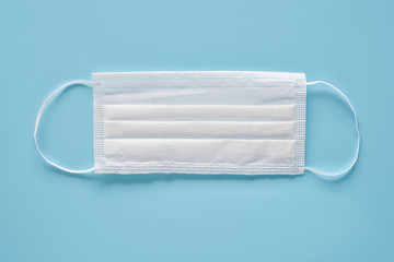 Obraz premium Medical mask on blue background. Typical 3-ply surgical mask to cover the mouth and nose. Procedure mask from bacteria. Healthcare and protection concept.