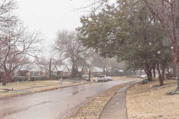 Fototapeta na wymiar Heavy snowfall over suburban residential street with row of bungalow houses and sidewalk in Coppell, Texas, USA