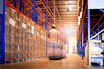 Interior of storage warehouse with tall shelves, forklift diver unloading pallet goods