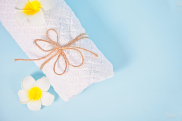 Care, beauty and spa concept. White towel and plumeria frangipani flower. Copy space. Top view.