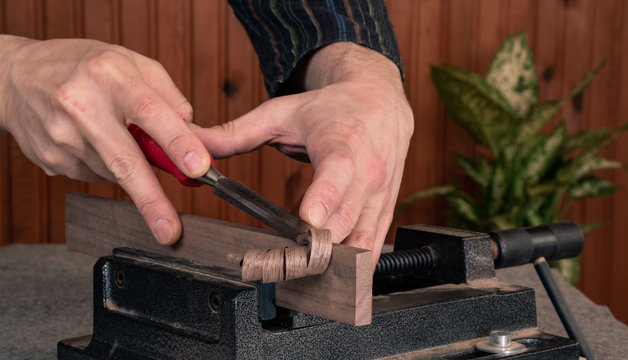 closeup scene of hands of a male wood worker, shaping wooden plank with chisel - locked in the vise