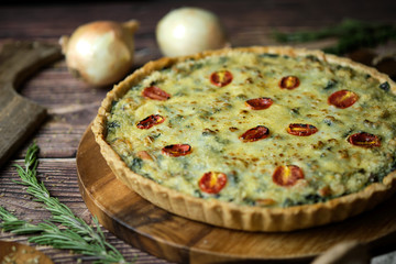 Homemade cheesy spinach quiche for brunch. set on wooden cafe table background.