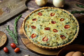Homemade cheesy spinach quiche for brunch. set on wooden cafe table background.