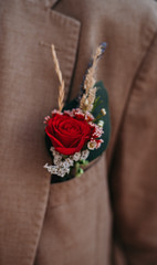 a small bouquet of red roses and dried flowers inserted into the pocket of a brown men's jacket