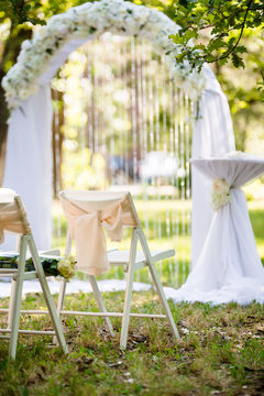 White luxury wedding ceremony decorations outdoor in the summer park. Table, chairs and weddinh decorated arch