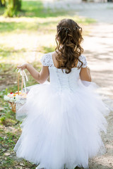 Fototapeta na wymiar Little girl in lace white dress holds a basket with petals on wedding ceremony