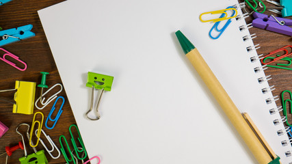 Smiles Binder Clips with School Office Supplies. Paper notebook with green pen. School stationery on brown wooden table. Concept of back to school, education or knowledge