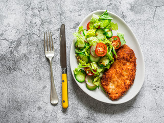 Chicken schnitzel and fresh cherry tomatoes, cucumbers, radishes, romaine salad on a gray...
