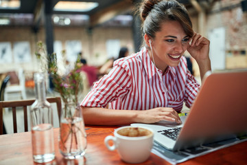 Woman using laptop in cafe.Girl sitting at a cafe,laughing and enjoying at coffee.