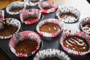 
A muffin baking dish in which there are paper inserts with chocolate dough inside. Homemade cakes for children and adults