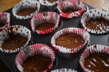 
A muffin baking dish in which there are paper inserts with chocolate dough inside. Homemade cakes for children and adults