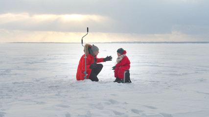 Dad and son are fishing in the winter. Long shot