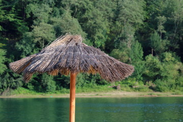 Fototapeta na wymiar reed beach umbrella close up, in background sea lake and green forest, concept of tourism close to nature 