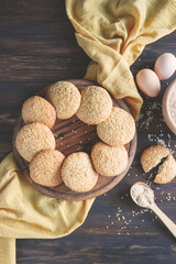 Sesame biscuits, homemade healthy snack. Honey bars with sesame seeds on old wooden board with ingredients for cooking -  eggs, flour on rustic table. Top view, flat lay, copy space.